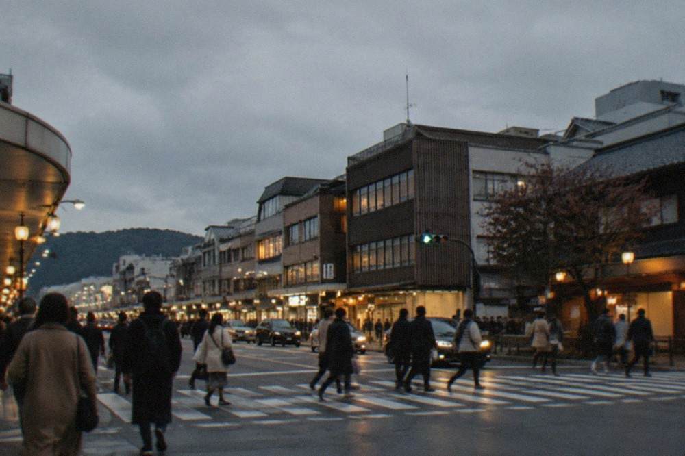 Shoppers crossing a busy downtown Kyoto intersection at dusk under illuminated shopfronts