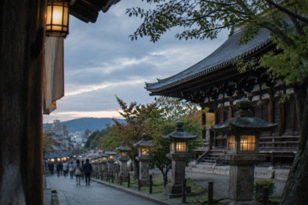 A wooden temple hall and stone lanterns along a path in Nara Park on a bright afternoon