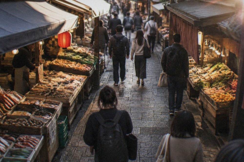A covered market lane with food stalls on both sides and shoppers walking between them