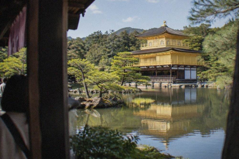 The gold-leafed Kinkaku-ji pavilion reflected in the pond beside it, with pine trees at the water's edge