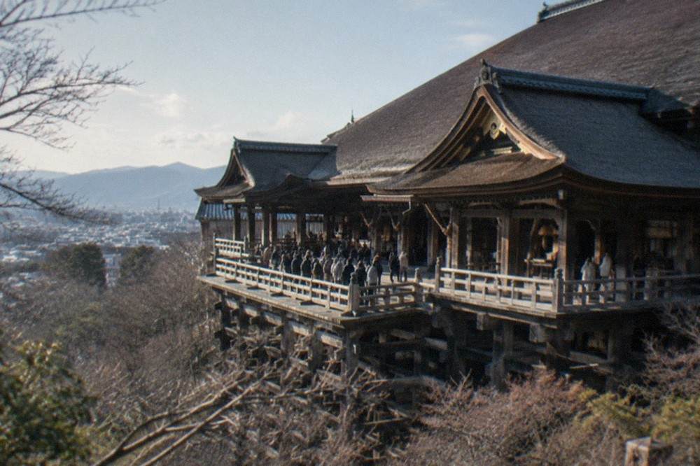 A long wooden temple hall seen from outside, with visitors gathered near the entrance on a clear day