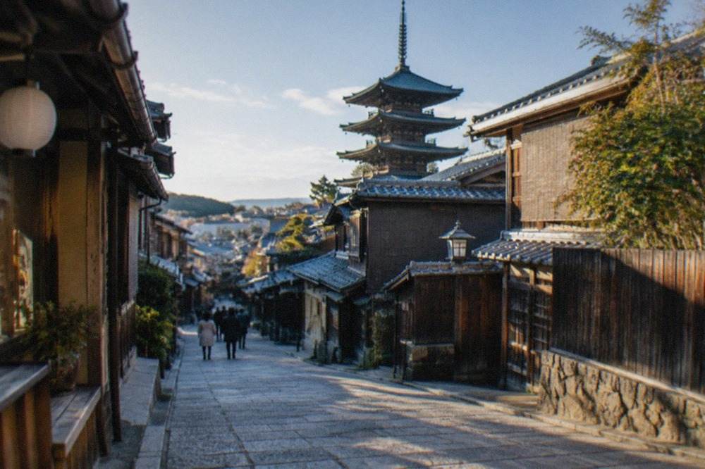 Stone-paved slope in Higashiyama with traditional wooden machiya shopfronts and a pagoda rising behind them