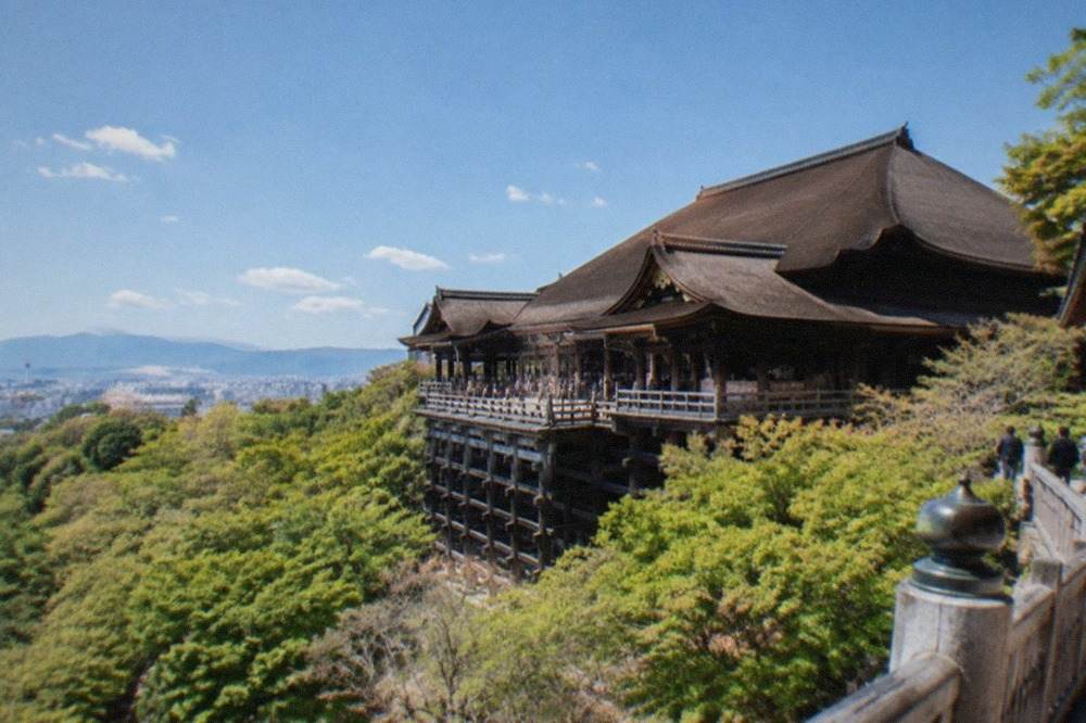 The wooden main hall of Kiyomizu-dera standing on tall pillars above a tree-covered hillside
