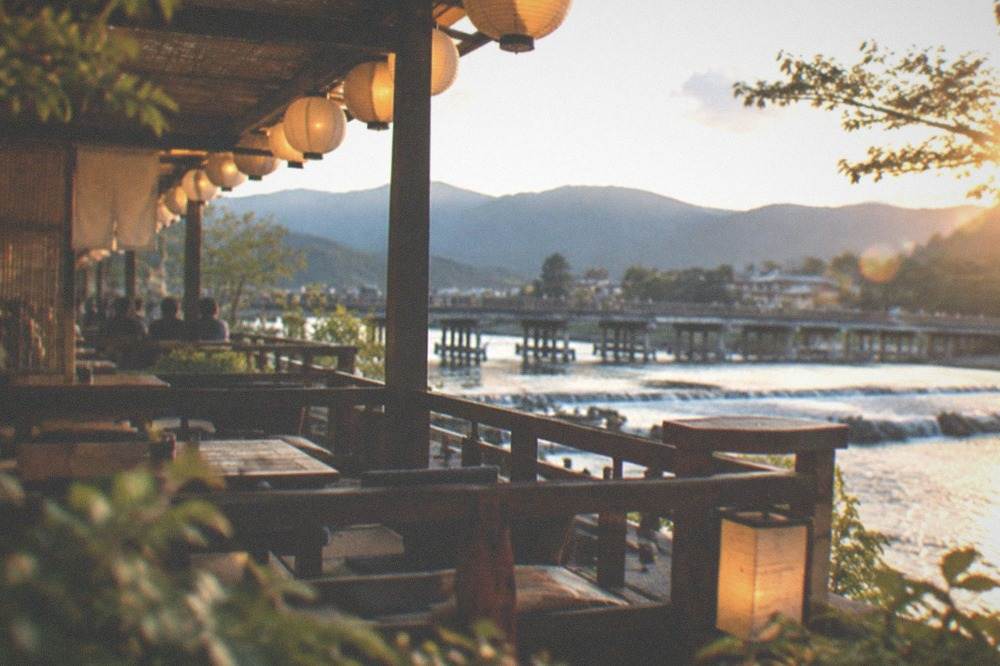 A wooden restaurant terrace overlooking a river with lanterns lit in the late afternoon