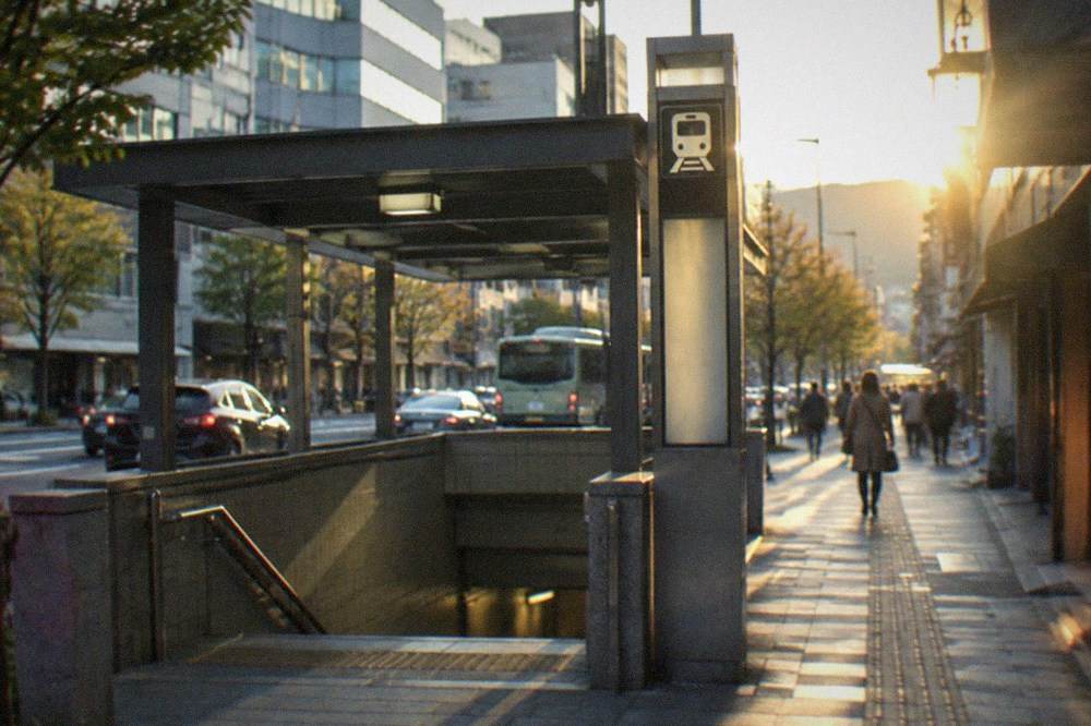 A subway entrance on a wide downtown Kyoto boulevard with office towers and a station sign