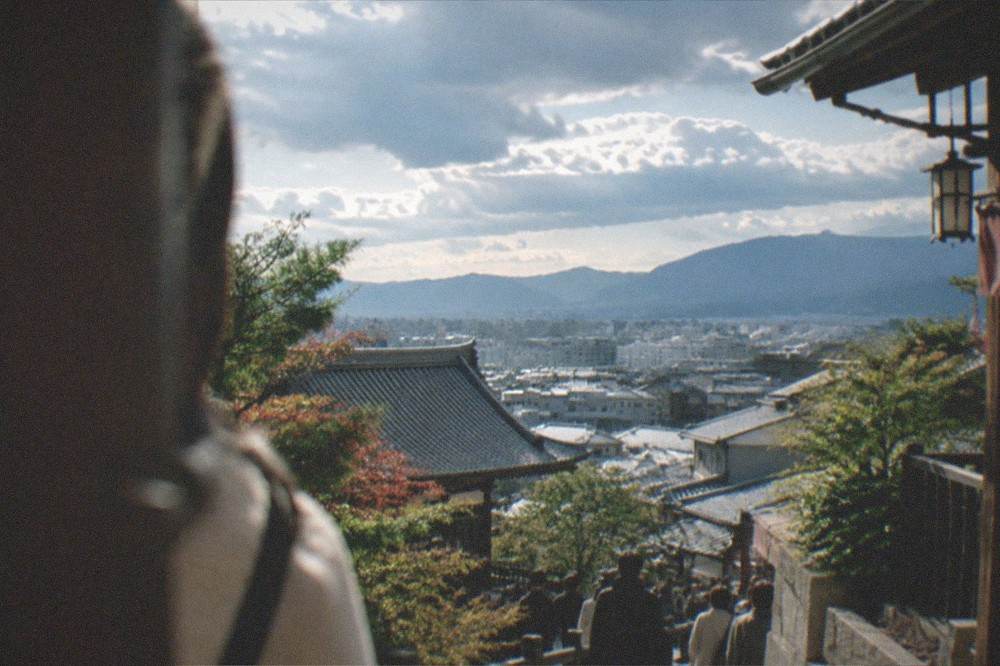 Wide view over Kyoto rooftops from a hillside temple terrace with the eastern mountains beyond