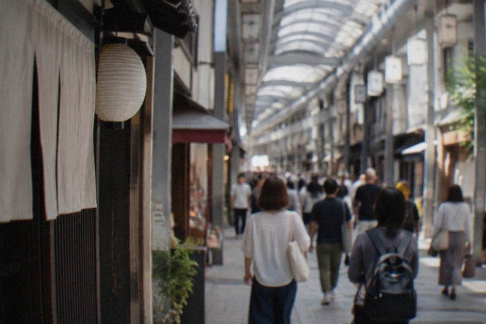 A covered shopping arcade in Kyoto with small shopfronts and pedestrians walking under the roof