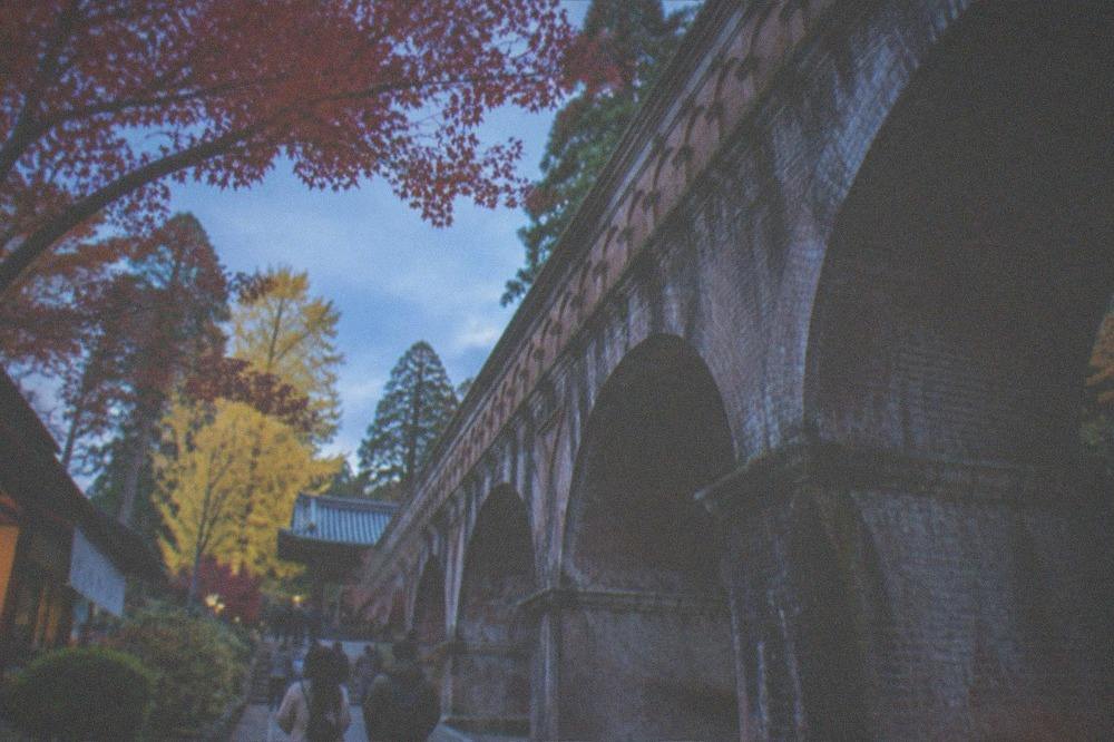 A brick aqueduct carrying a canal through temple grounds with autumn trees