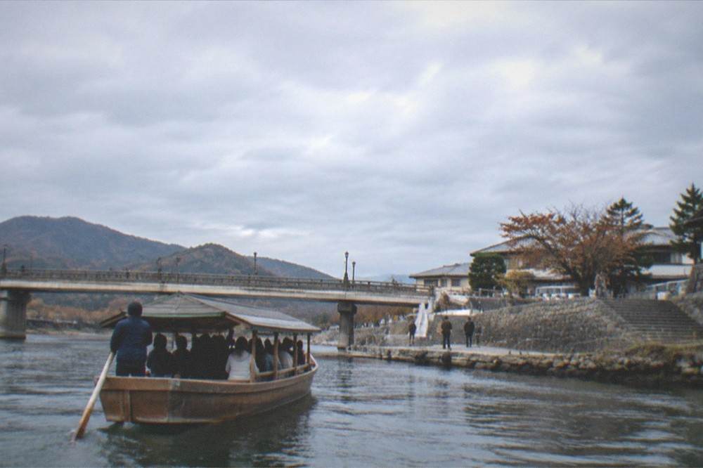 A wooden river boat approaching a stone landing near a bridge in late afternoon light