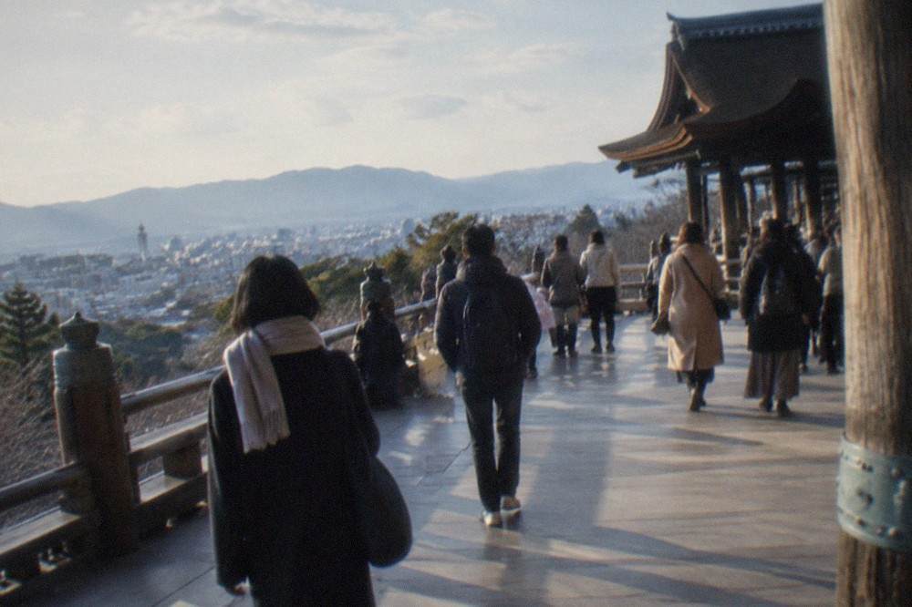 Visitors crossing the wooden stage of Kiyomizu-dera with the city of Kyoto spread out behind them