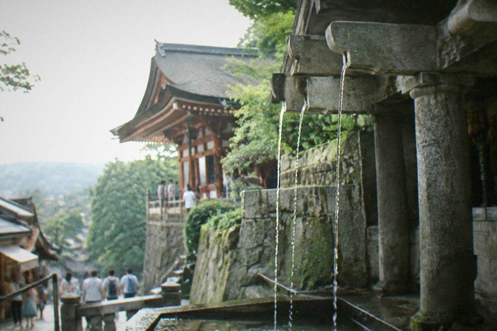 The three thin streams of the Otowa waterfall falling into a stone basin below the temple hall