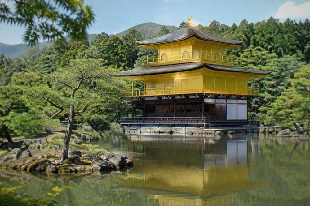 A golden pavilion reflected in a still pond surrounded by trees