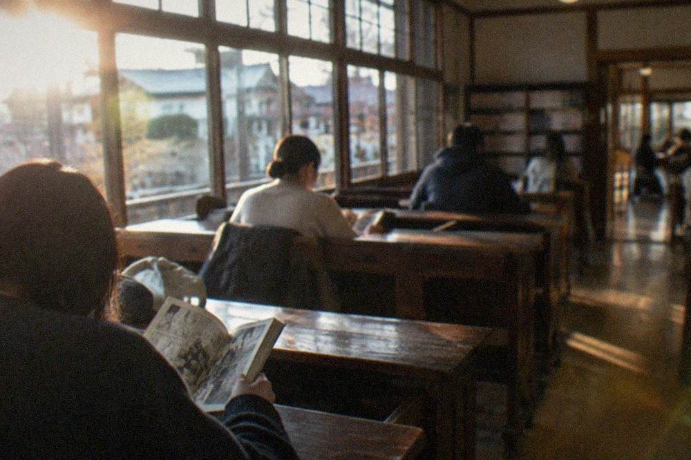 Visitors reading manga at wooden desks inside the museum's former classrooms
