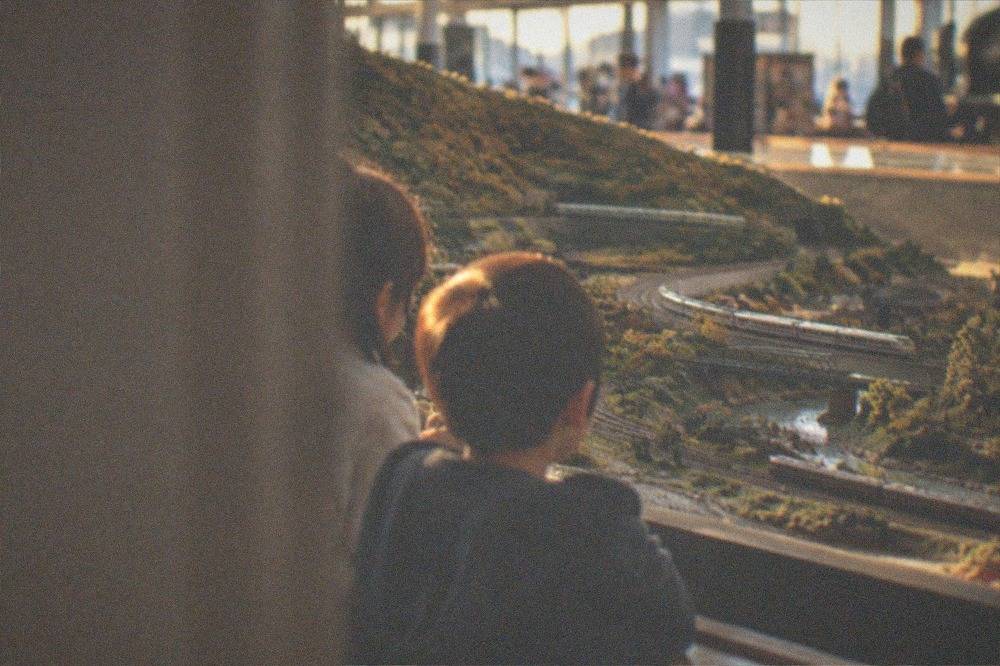 Children watching a model railway diorama with tiny trains moving through a miniature landscape