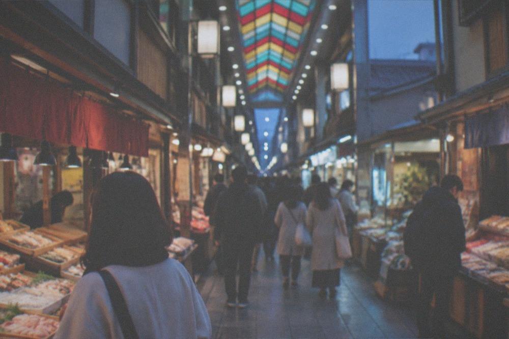 Shoppers browsing a busy covered market lane with food displays on both sides