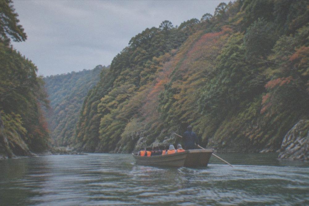 A flat-bottomed wooden river boat with passengers in life vests passing between steep forested banks