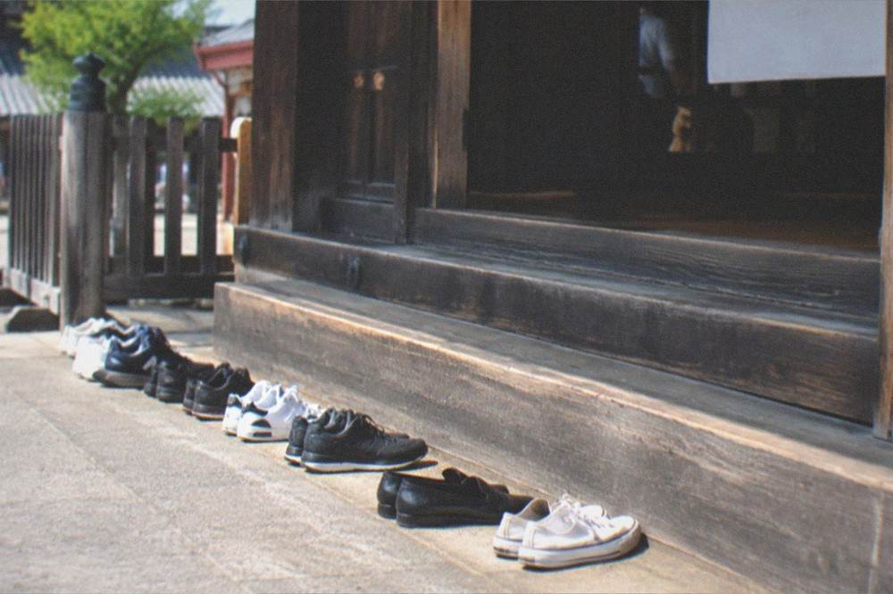 A row of shoes left at a wooden temple step before entering a hall