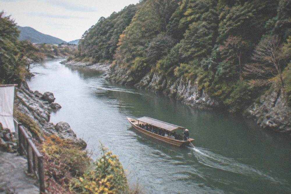 A wooden passenger boat drifting between forested cliffs on a river
