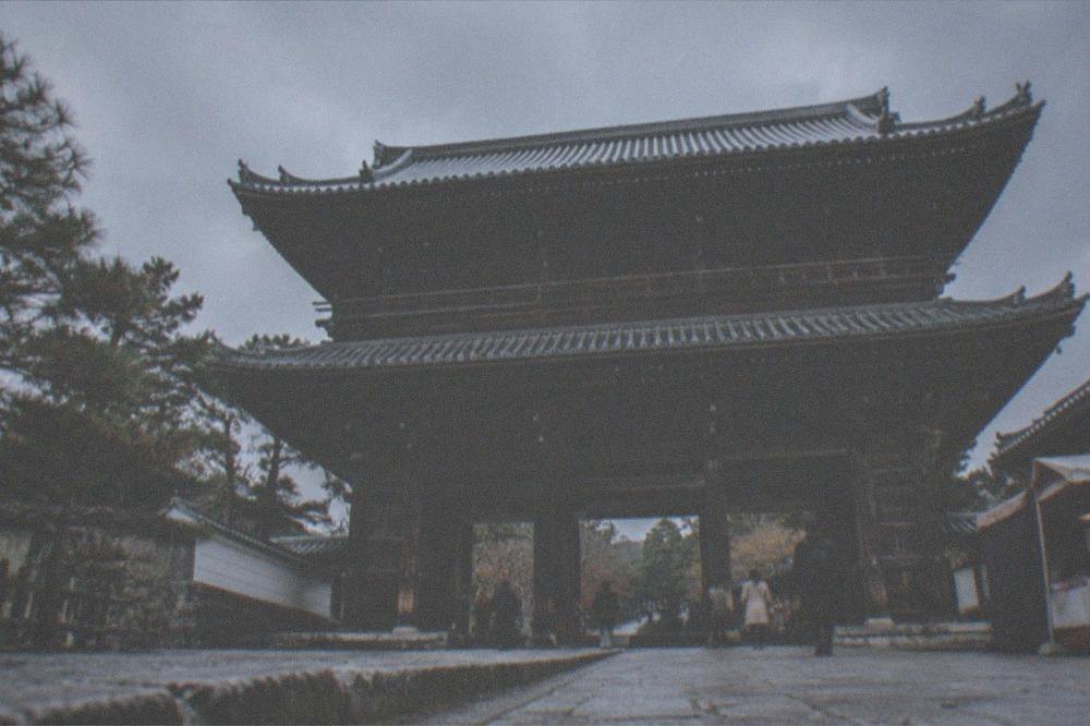 A large two-storey wooden temple gate with tiered roofs seen across a stone courtyard
