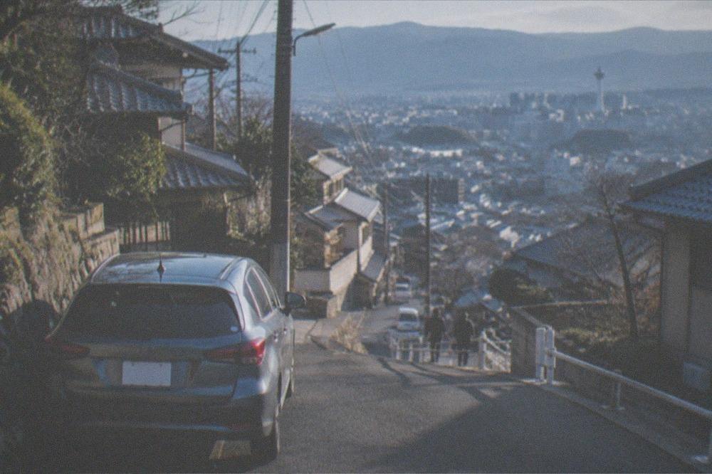 A private car parked on a narrow mountain road above Kyoto with the city spread out below