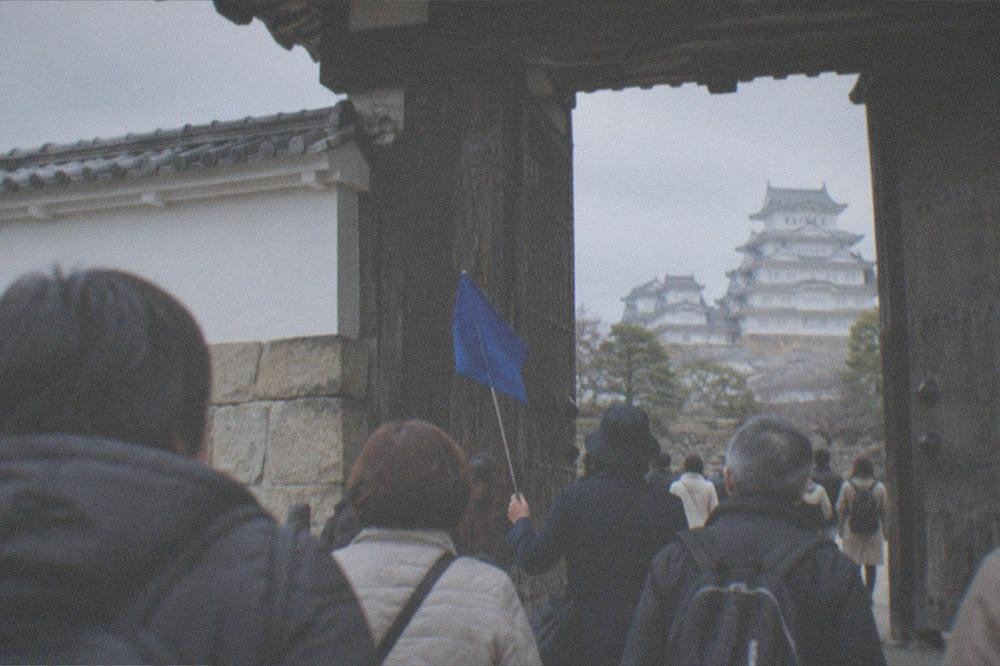 A tour group with a guide holding a flag walking through a Japanese castle gate