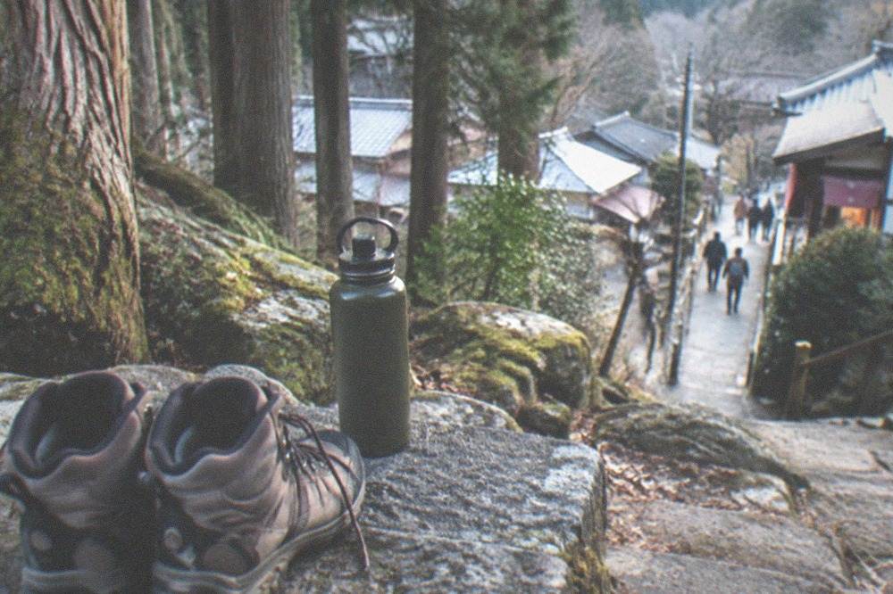 Hiking boots and a water bottle on a stone step beside a cedar forest
