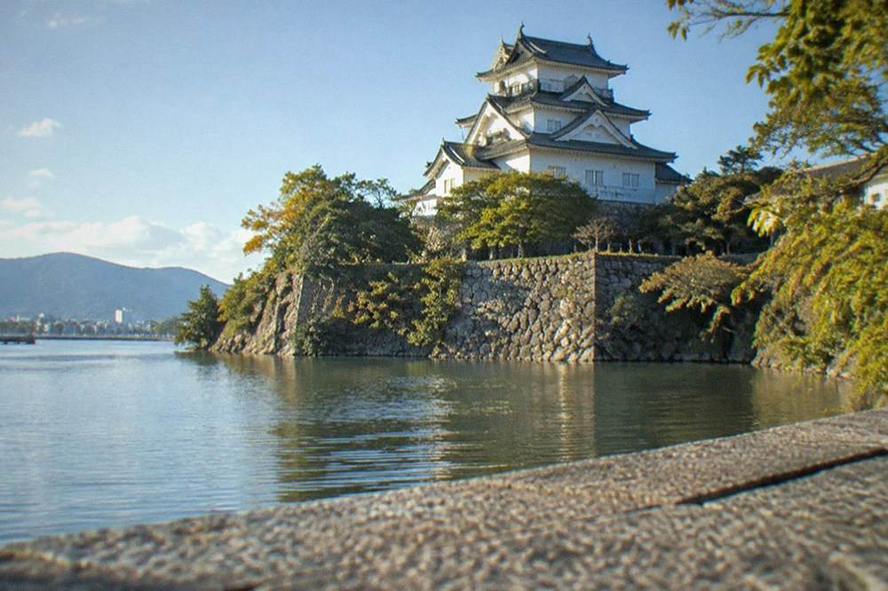 A white Japanese castle keep on a hill above a lake with a moat in the foreground