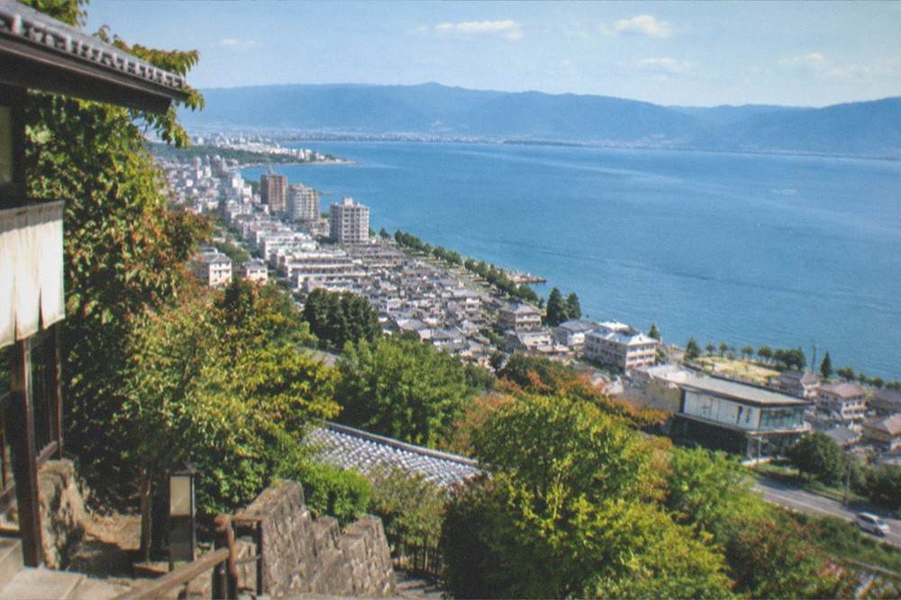 A wide lake seen from a hillside viewpoint with a town along the shoreline below