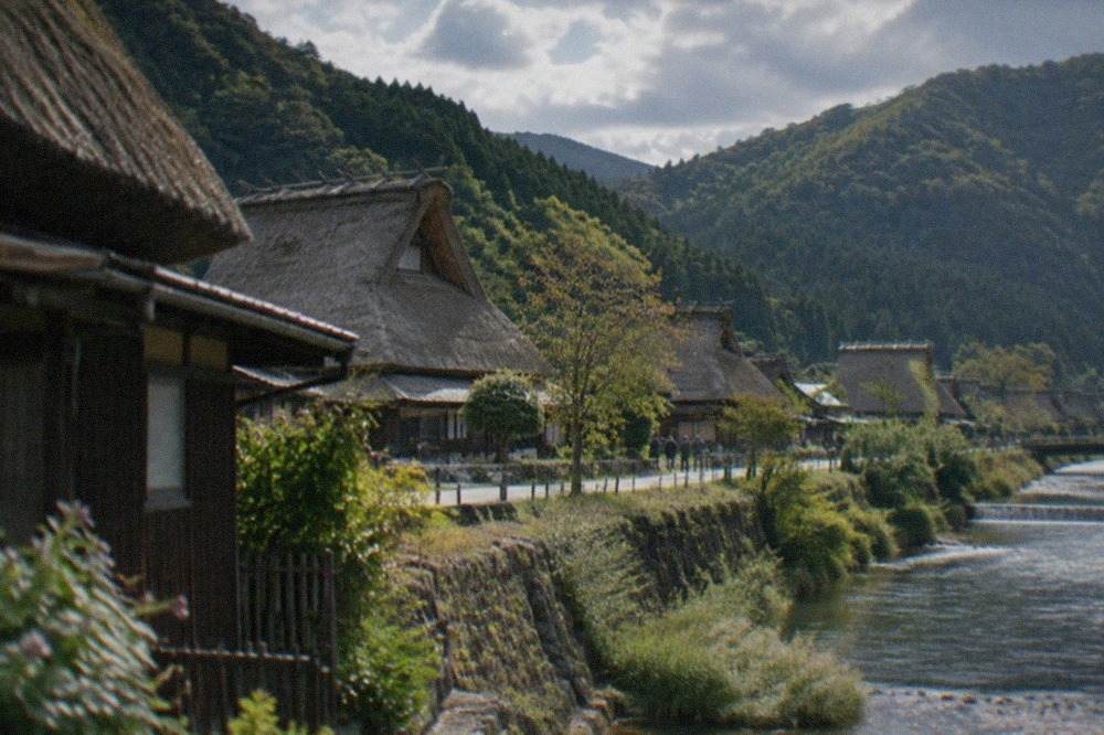 Thatched farmhouses with steep roofs standing along a river in a green mountain valley