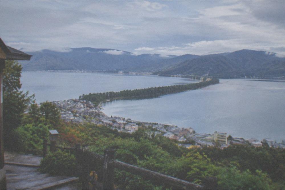 A sandbar lined with pine trees seen from a mountain viewpoint above a coastal bay
