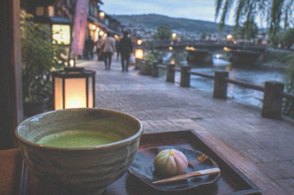 A bowl of bright green matcha tea and a small sweet on a wooden tray