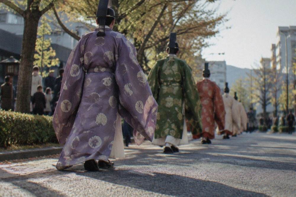 Costumed procession participants in Heian period robes walking a tree-lined Kyoto street
