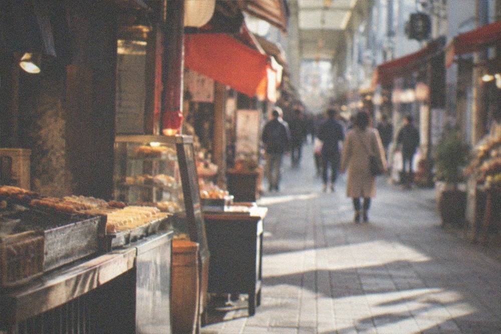 A narrow covered shopping arcade in Kyoto with food stalls and small restaurant signs on both sides