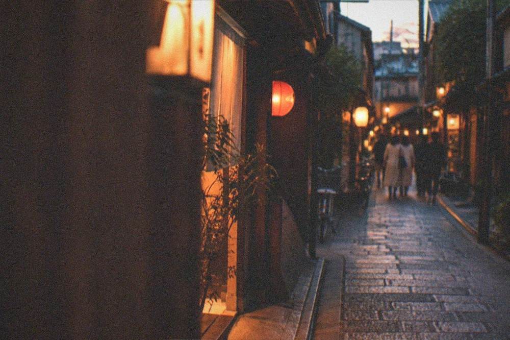 A quiet Kyoto alley at night with warm light spilling from small restaurant doorways