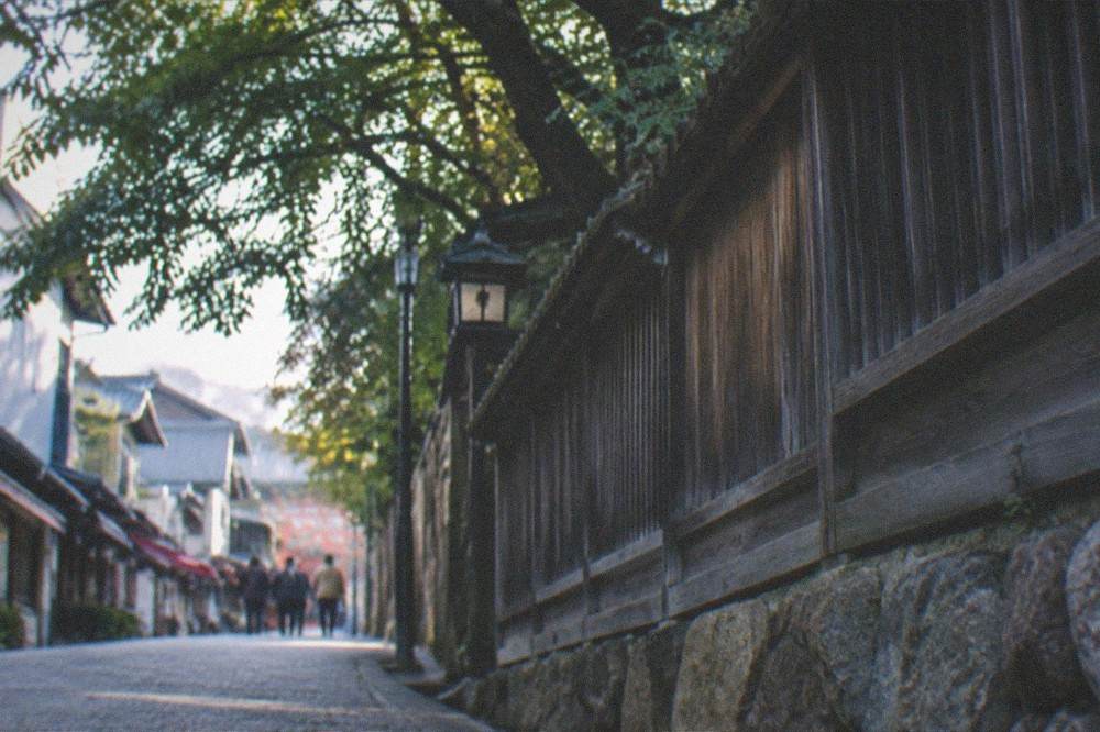 A quiet stone path beside a wooden temple fence in Kyoto with morning light through the trees