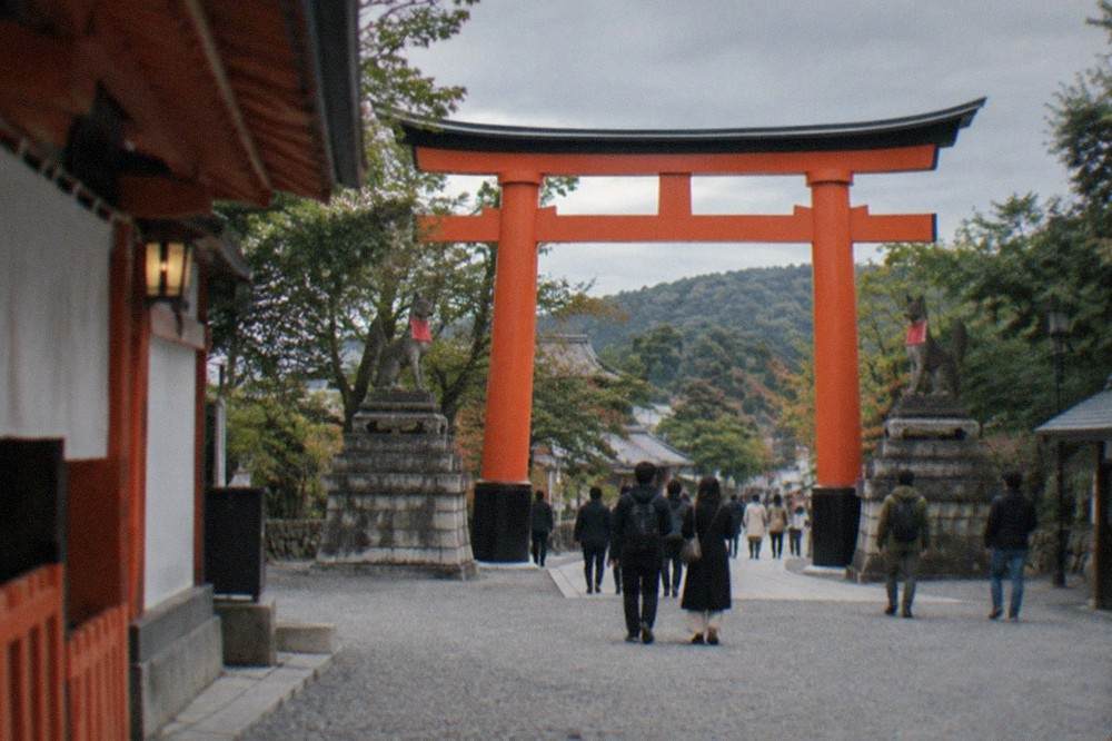 The wide gravel entrance approach to Fushimi Inari Taisha with the large torii gate and fox statues
