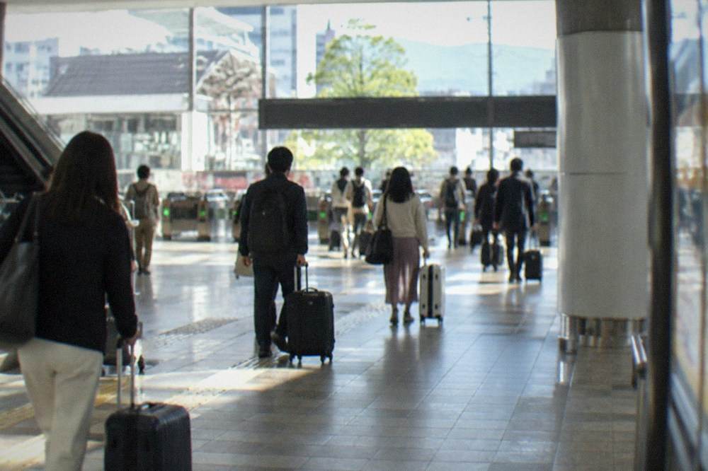 Travelers with suitcases walking through a bright airport station concourse toward ticket gates