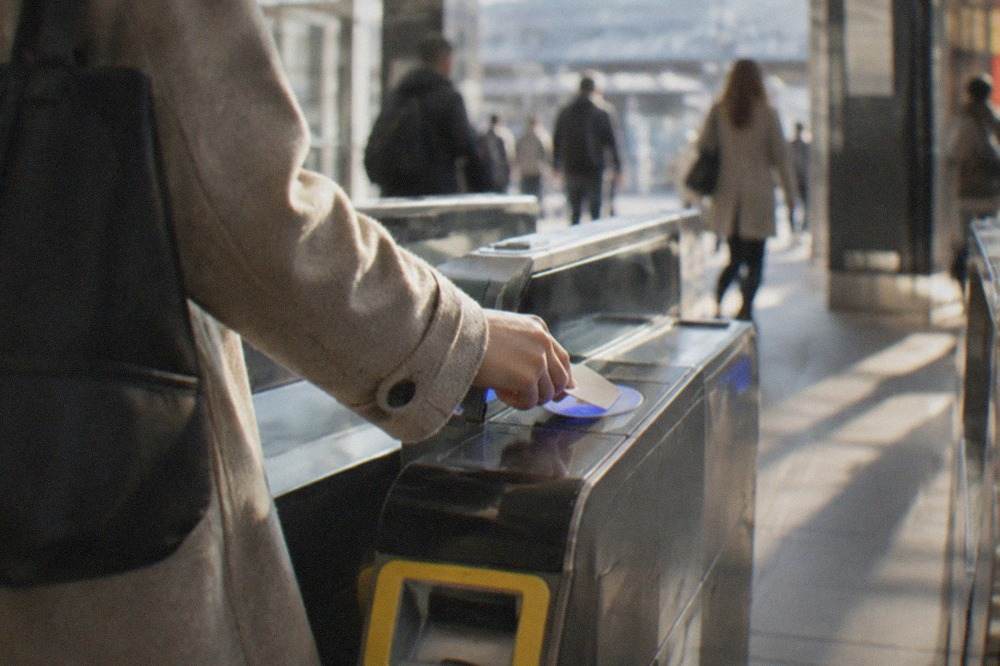 A commuter tapping a smart card on a ticket gate reader at a Kyoto railway station