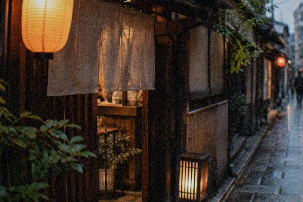 A warm lantern-lit izakaya entrance on a narrow Kyoto street at dusk