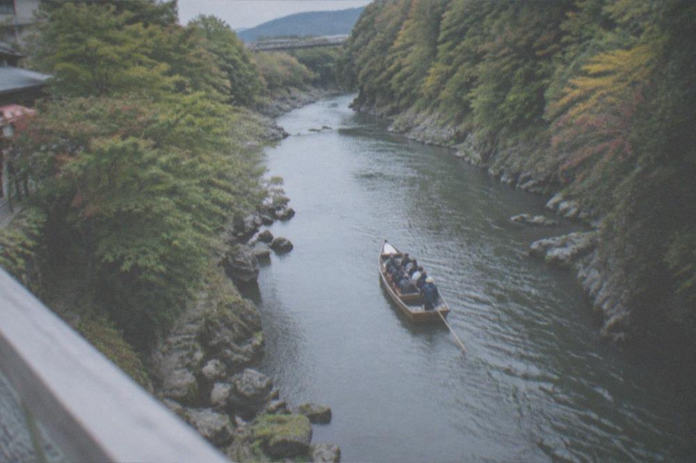 A small open boat carrying passengers down a forested river gorge