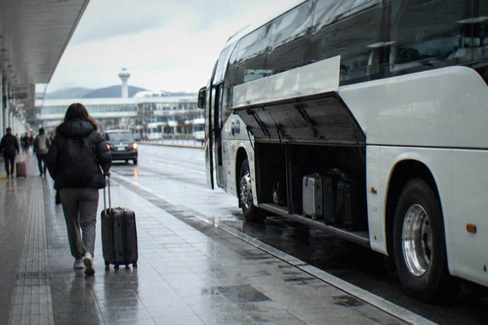 A highway coach parked at an airport curb with luggage bay doors open