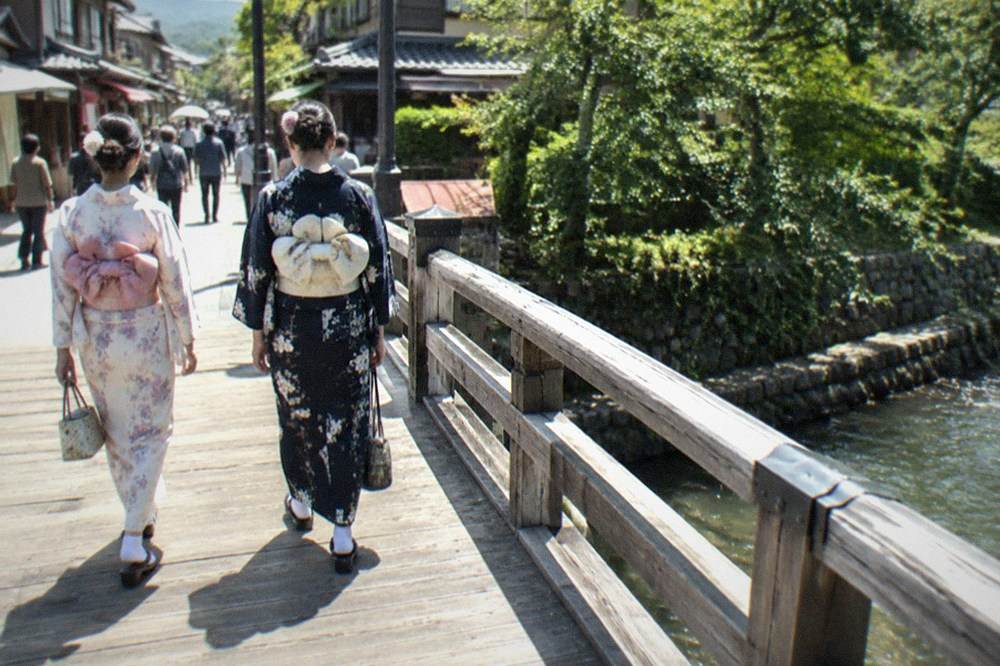 Two visitors in kimono crossing a wooden bridge in the Arashiyama district