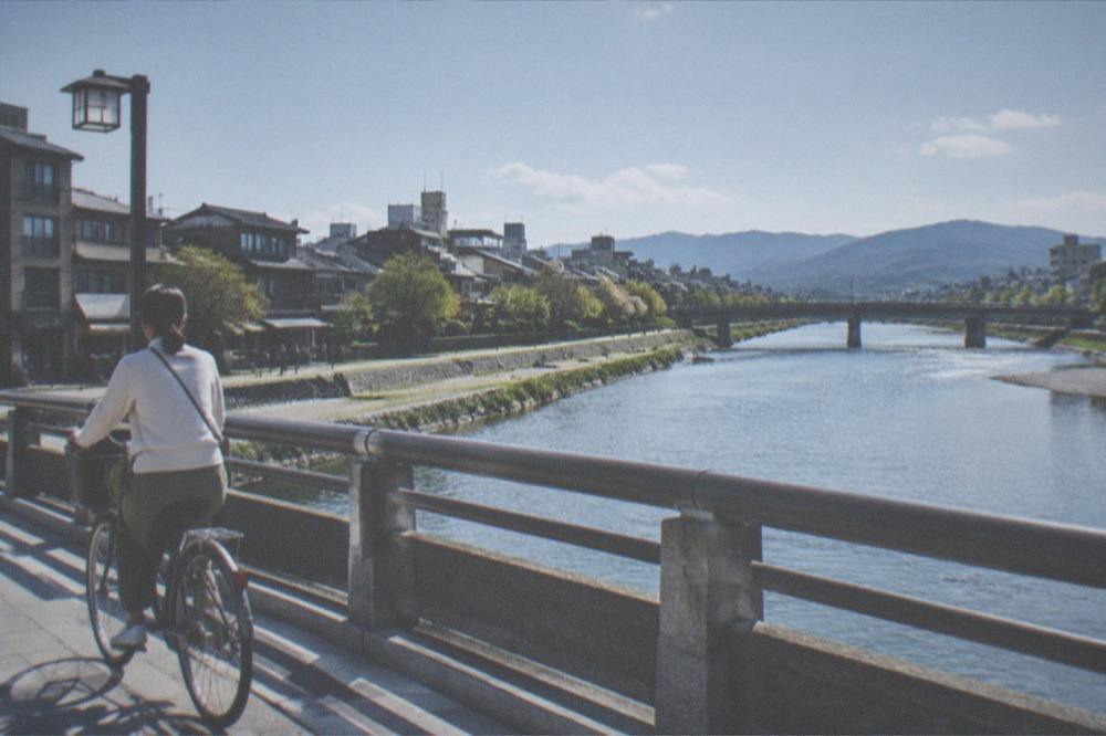 A cyclist crossing a bridge over the Kamo River in soft morning light
