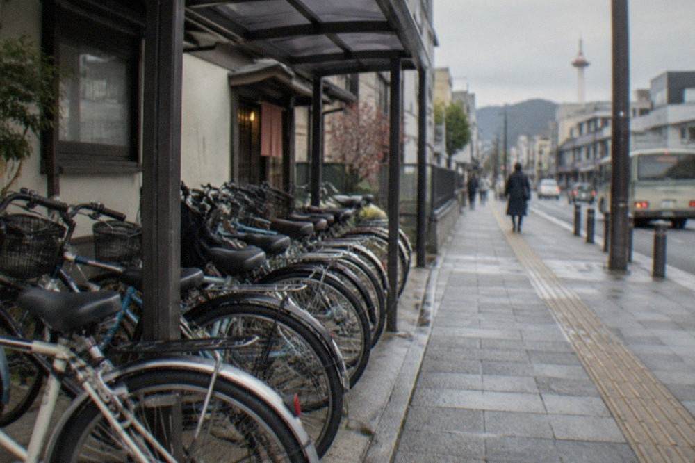A row of rental bicycles parked in a covered row outside a small Kyoto shopfront