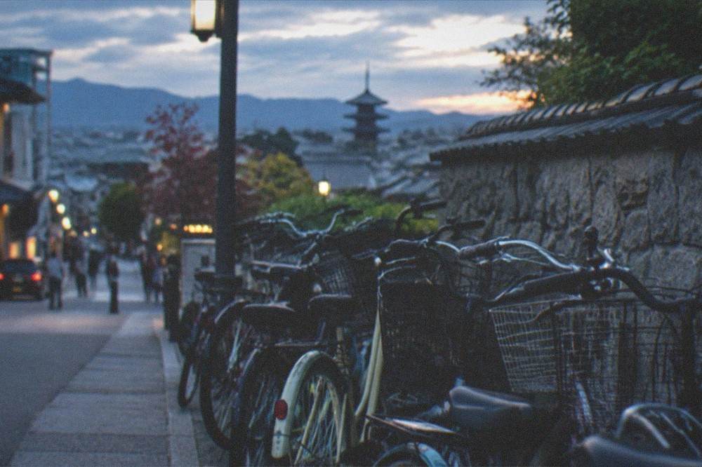 Bicycles parked in a neat row beside a stone wall as evening light falls over Kyoto rooftops