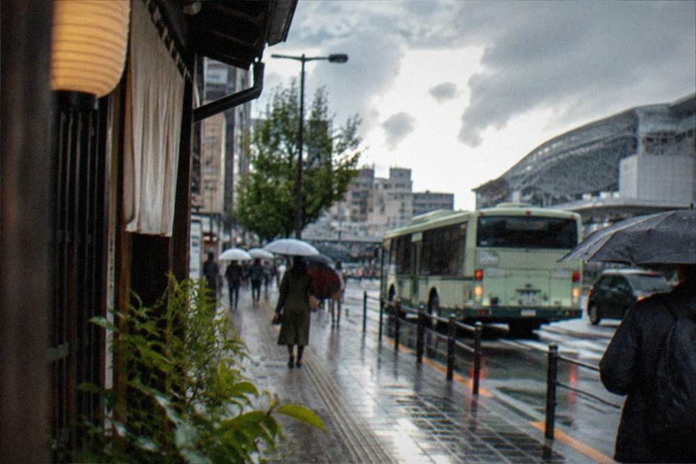 Rain falling on a Kyoto street with a bus and umbrellas visible