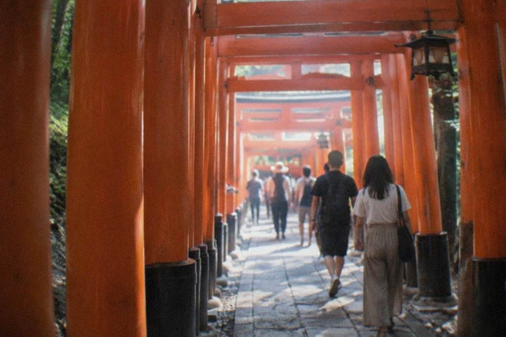 Visitors walking through the dense tunnel of red torii gates on the Fushimi Inari mountain path in Kyoto