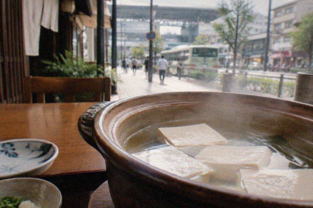 Blocks of fresh tofu simmering in a clay pot of clear kombu broth on a restaurant table