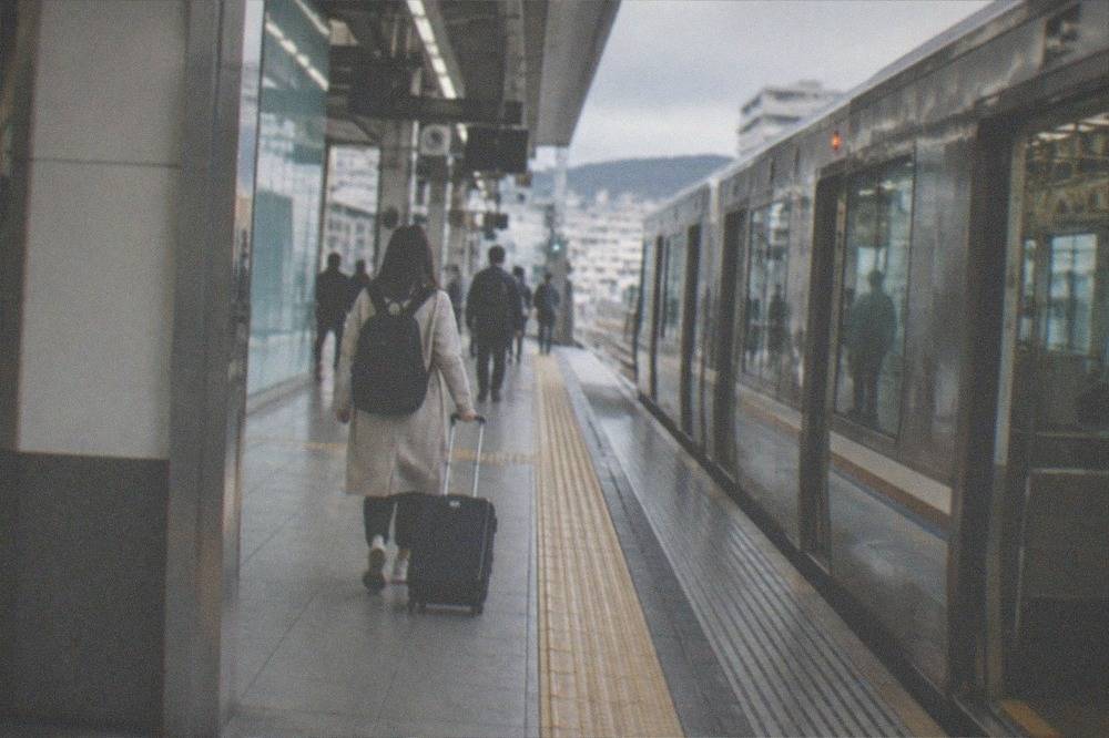 A subway platform in Kyoto with a traveller wheeling a suitcase toward the train