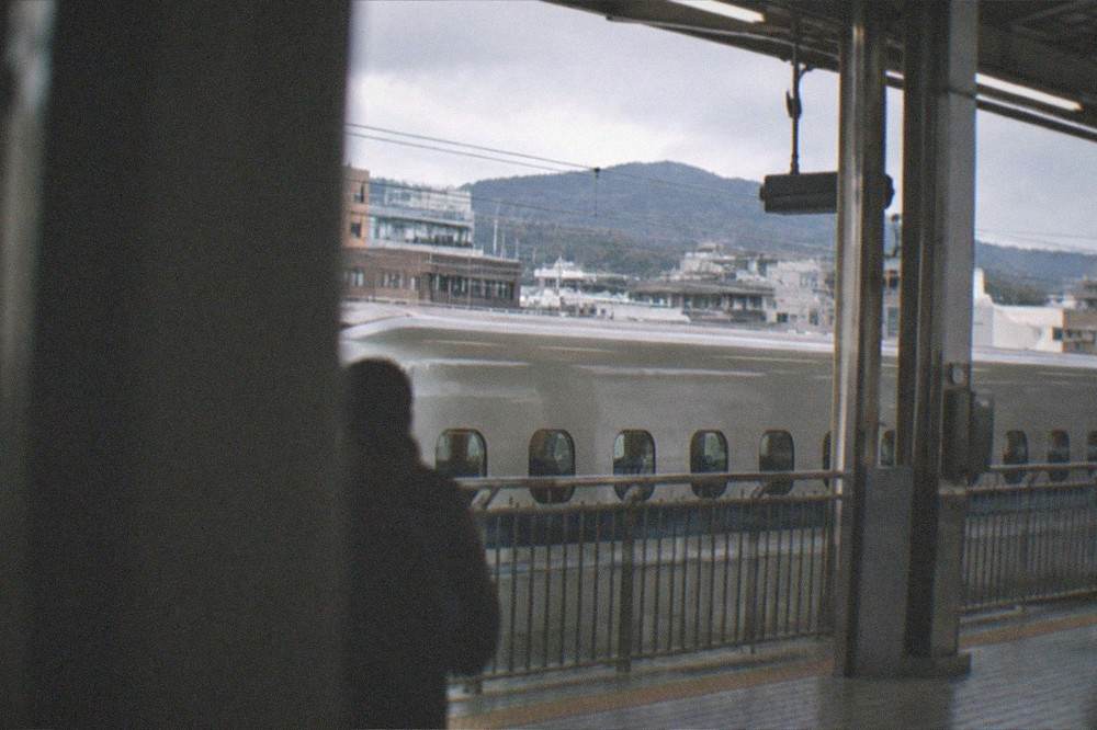 A rapid train waiting at a platform with hills beyond the station